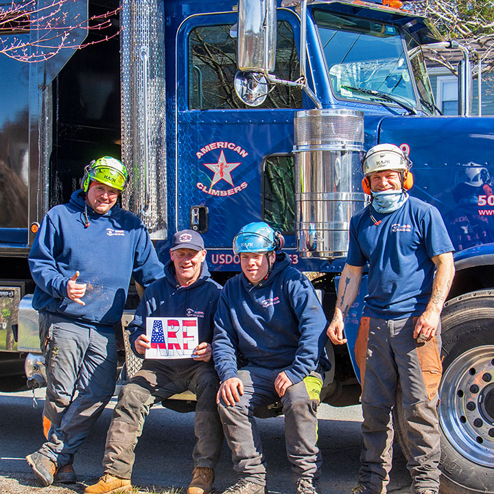 Four members of the American Climbers tree care crew in front of a blue truck.