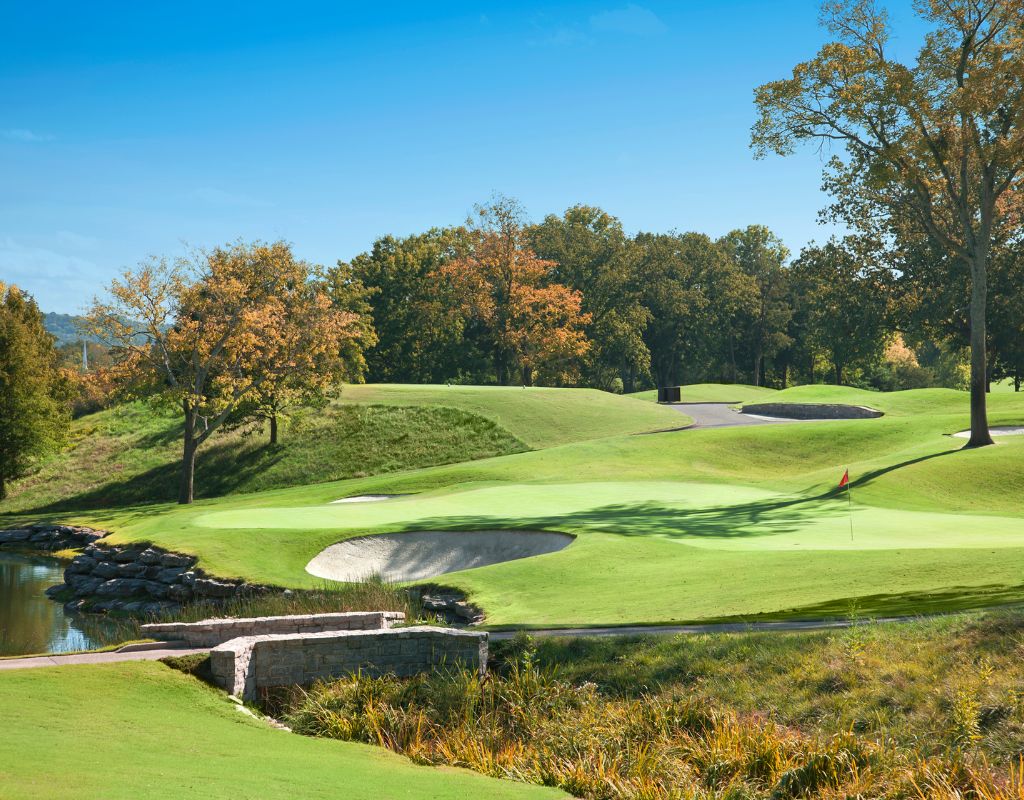 A golf course with rolling hills, water, and colorful fall trees.