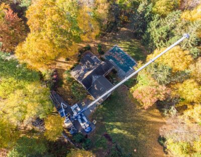 An old home surrounded by trees with roots that are damaging the foundation in framingham, ma. The american climbers team is using a crane to remove the offending trees.