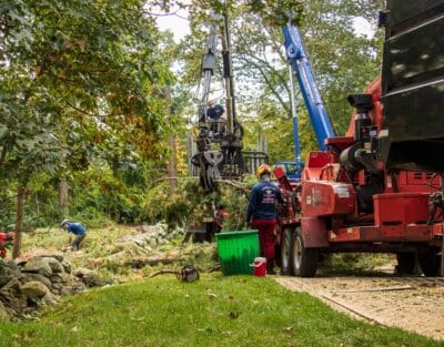 Tree removal crew operating a crane and wood chipping equipment to remove and process a large felled tree from a residential property