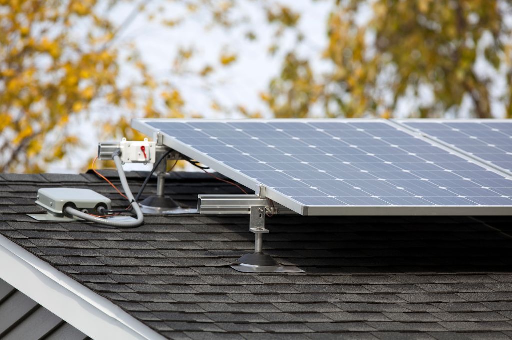 Solar panels mounted on a home roof with trees in the background.
