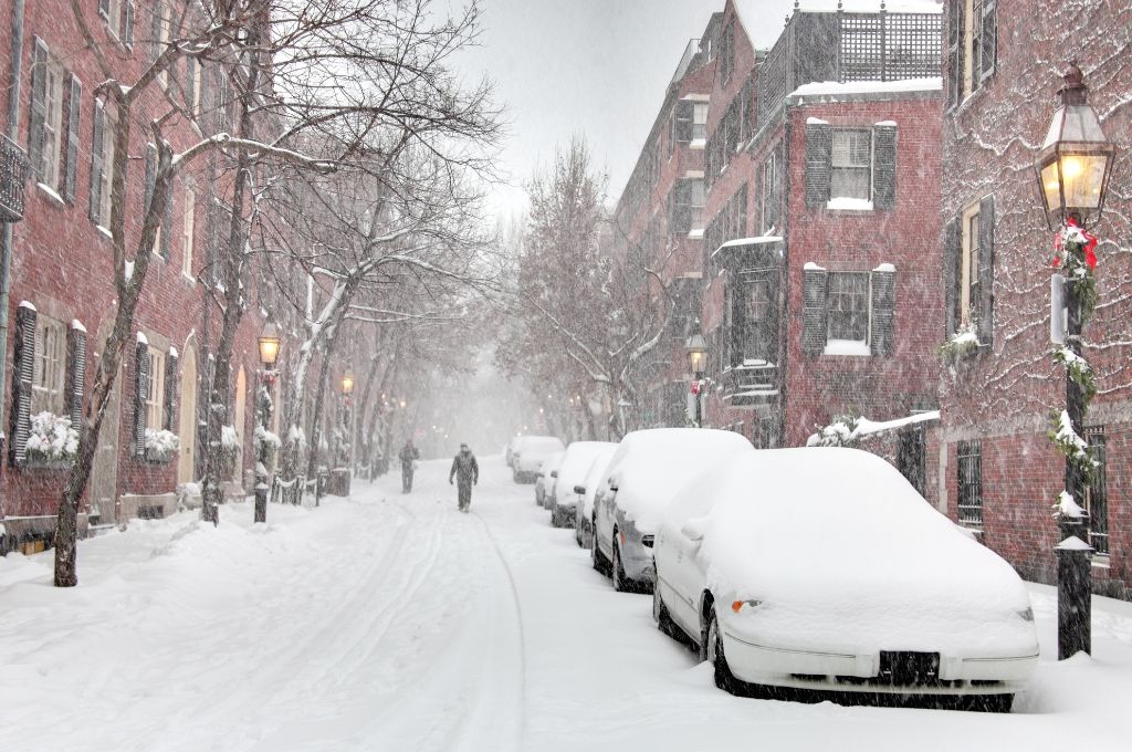 A snow-covered residential street with buried cars during a winter storm in massachusetts.
