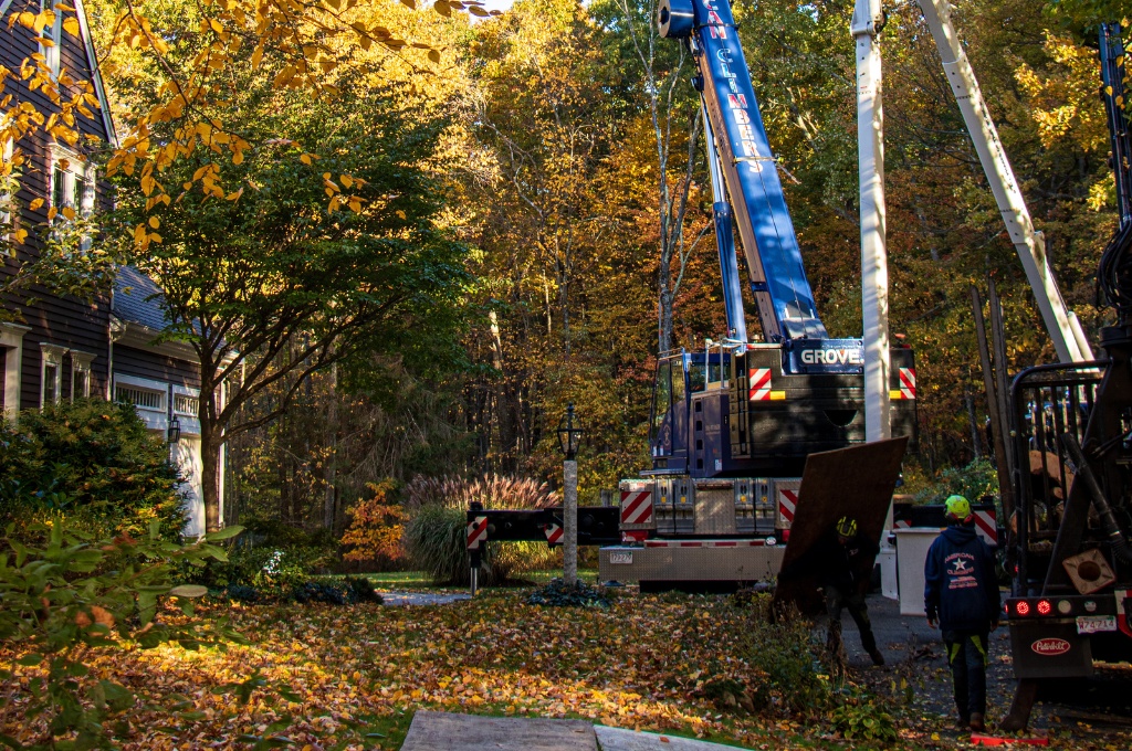 The american climbers blue crane truck performing professional tree removal in a metrowest massachusetts residential neighborhood during the fall season.