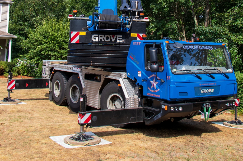 Will a Crane Damage My Property? MetroWest Homeowner's Guide to Crane-Assisted Tree Removal American climbers crane setup in wooded area with outrigger pads deployed on natural ground for tree removal operation.