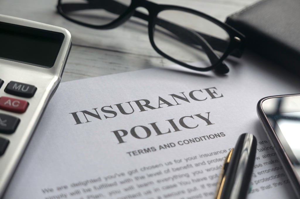 An insurance policy document sits on a desk next to a calculator, reading glasses, and a pen.