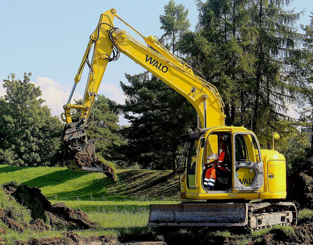 Construction equipment on tilled soil with trees and green lawn in the background