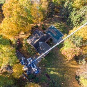 An old home surrounded by trees with roots that are damaging the foundation in Framingham, MA. The American Climbers team is using a crane to remove the offending trees.
