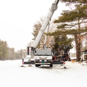 A professional tree removal crane positioned for winter tree work in a snow-covered residential area.